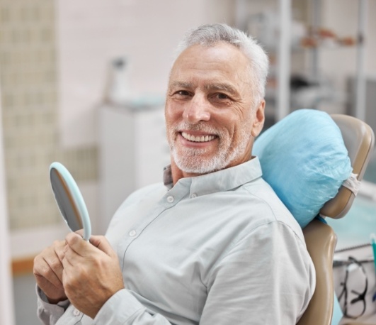 Senior man smiling and holding mirror in dental chair